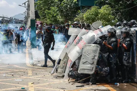 AFP via Getty Images Armed Police Force (APF) personnel stand guard during a protest outside parliament