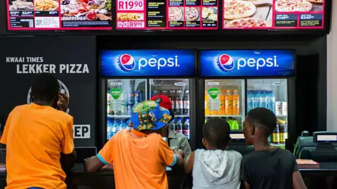 Getty Images Four boys, two in orange t-shirts, stand at a pizza fast food counter ordering food with two drinks machines advertising Pepsi in the background 