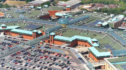 Meadowhall An aerial shot of a large building with a glass dome with a car park surrounding it. 