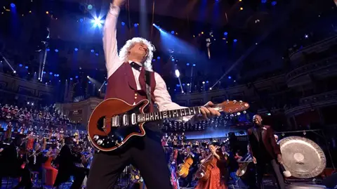 Brian May thrusts his hand into the air after playing the guitar solo from Queen's Bohemian Rhapsody