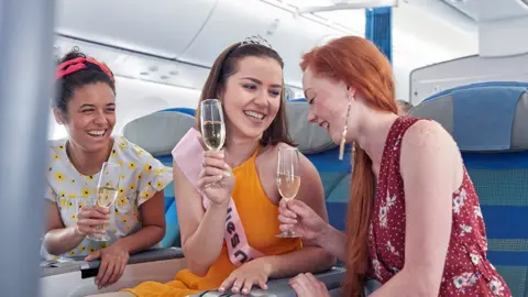 Getty Images Young women friends laughing, drinking champagne on airplane