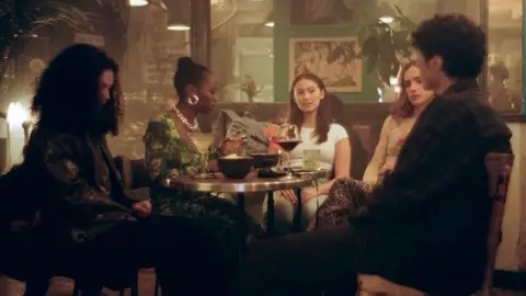 Prime Video A scene from The Summer I Turned Pretty - cast members sit around a table in a bar with drinks laid out