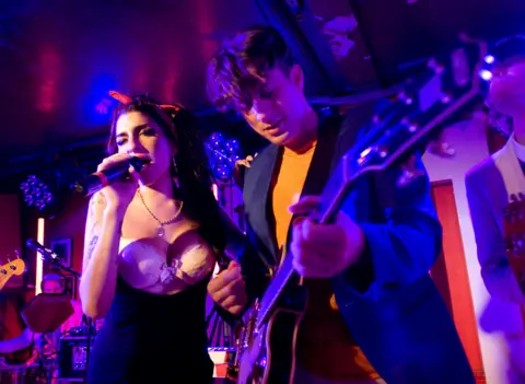 Getty Images Mark Ronson playing guitar next to Amy Winehouse singing into a microphone on stage