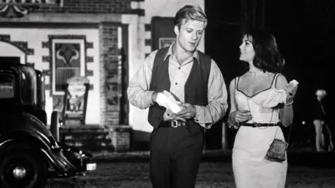 Getty Images Robert Redford and Natalie Wood in a black and white still from Inside Daisy Clover.  They are walking together outside.