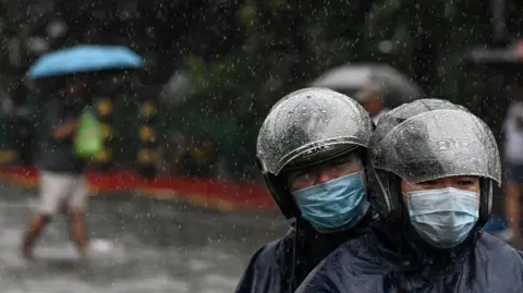 Getty Images A couple wearing helmets riding a motrbike under the rain