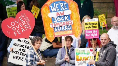 PA Media A woman holding a sign displaying the message: 'we're aw Jock Tamson's bairns'.