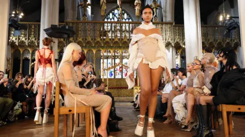 EPA A model wearing white walks a makeshift catwalk inside St Cyprian's Church, London. 