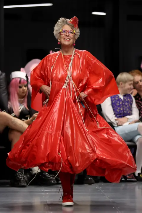 Getty Images Dame Prue Leith walking down the catwalk in a large red parachute style dress.
