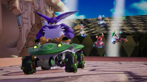 Sega Screenshot from Sonic Racing: Crossworlds shows Big the Cat - a large, purple feline, racing away from a pack of other characters, all of whom appear to be careening down a hill in the background.