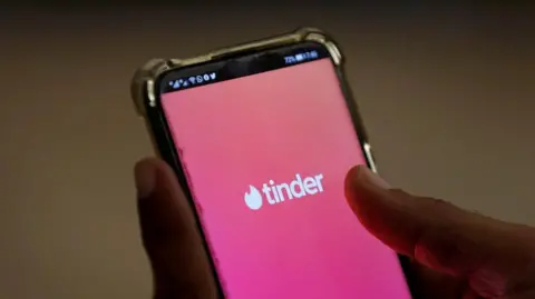 Reuters A close shot of a hand holding a smartphone with the pink background and logo of tinder dating app