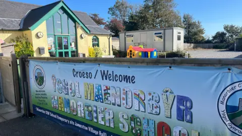 A banner shows the name of the school and its logo outside the village hall building