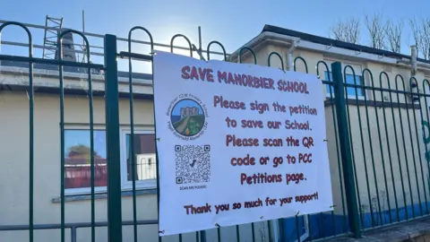 Exterior of Manorbier school with a printed banner asking people to sign the petition, with a QR code