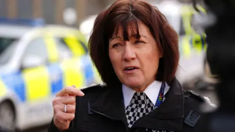 PA Media Jo Farrell, a woman with reddish-brown hair in a Police Scotland uniform, is standing talking to someone outside. A police car is in the background.