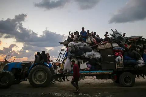 EPA A tractor tows a large truck filled with belongings and people. 
