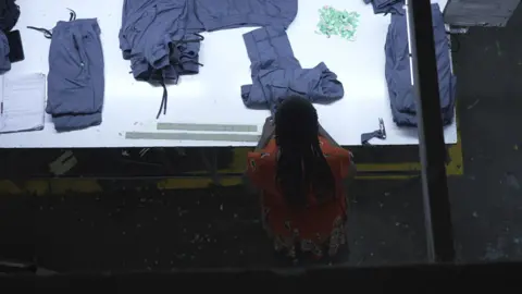 Hassan Lali / BBC Overhead image of a worker at a table inspecting finished garments.