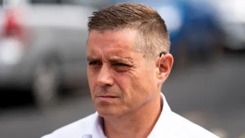 PA Media John Alford in a white shirt outside court, looking almost side-on. He is clean shaven. He has short hair, gelled into a quiff.