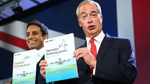 Getty Images Both are smiling and holding up signed copies of their new policy. The document pictures a plane coming to land on a runway, and reads Operation Restoring Justice. Behind them is the top left corner of a large union jack, that is the backdrop to where they are standing.