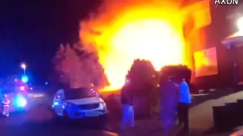 GMP A CCTV image showing a large orange and yellow glow outside a terraced house as neighbours and firefighters look on