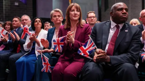 Reuters Labour ministers Shabana Mahmood, Yvette Cooper, Rachel Reeves and David Lammy clutch union jacks as they sit and watch Keir Starmer's conference speech