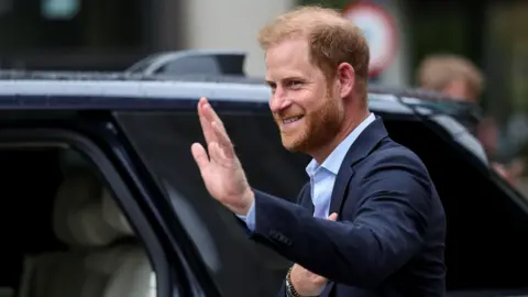 PA Media Prince Harry wearing a blue suit and blue shirt, waving as he steps into a black car.