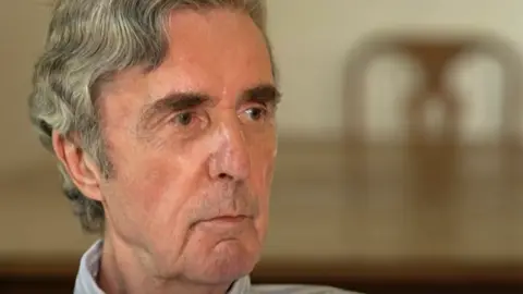 BBC Grey-haired John Stapleton speaking to the BBC in a TV studio