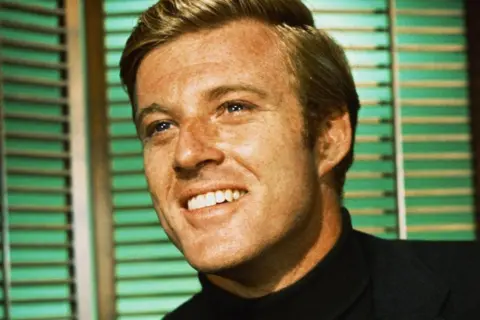 Getty Images Robert Redford is seen in his 20s. He is smiling radiantly and looking off to the left. 
