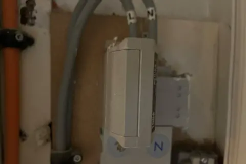 A grey box on a wall with wires coming in and going back out.