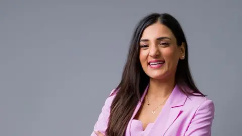 Anastasia Jobson With long dark hair and wearing a pink jacket, Dr Suglani smiles looking into the camera .