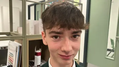 Shea (short dark hair) a green blazer and tie smiles at the camera