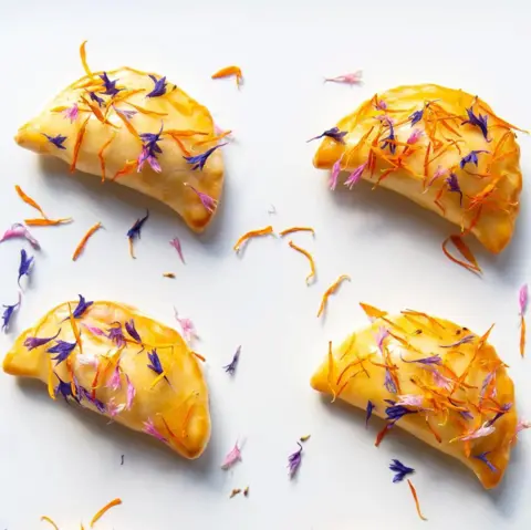 Catriona Byers Pastries laid out on a white surface and garnished with blue, pink and orange leaves. 