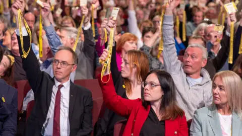 PA Media SNP members voting on independence strategy. Kate Forbes is in the middle in a red jacket holding a yellow pass.