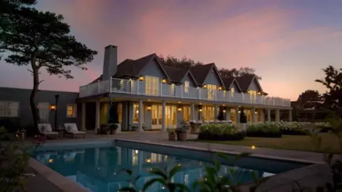 Omaze A nighttime image of Larkfields, used in the Omaze marketing campaign. The image is set over the swimming pool, looking to the rear of the house, with an evening sunset sky above.
