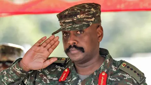 Getty Images Gen Muhoozi Kainerugaba salutes at a military drill competition. He is wearing  military fatigues - his epaulettes show he is a four-star general 