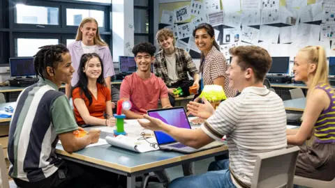 Getty Images Seven students are sitting around a table. They are with a teacher inside a classroom 