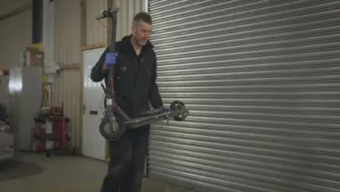 A police officer carries an e-scooter