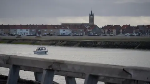 Lea Guedj/BBC A view of the canal at Gravelines with houses and a church in the background.