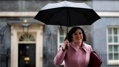 PA Media Bridget Philipson walking out of downing street smiling and holding an umbrella and a wearing a dusty pink coat.