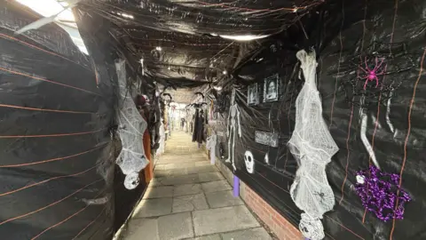 Paula Dewar A footpath with Halloween decorations on either side, including upside down skeletons and fake spiders, painted bright pink. 