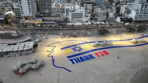 Reuters A giant sign created on a Tel Aviv beach reads "thank you" in blue and red and features an Israeli flag, as well as the outline of the profile of US President Donald Trump's head