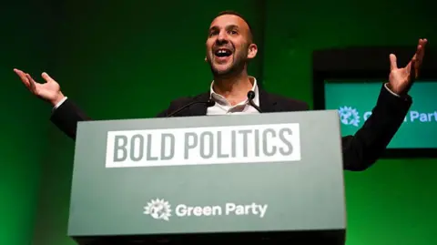 Getty Images Green Party leader Zack Polanski stands with his arms outstretched as he delivers his speech on the first day of the Green Party Conference in front of a sign saying "bold politics".