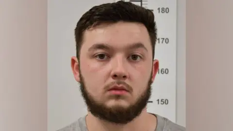 PA Media Dylan Earl wears a grey shirt and blank expression with short brown hair and a beard