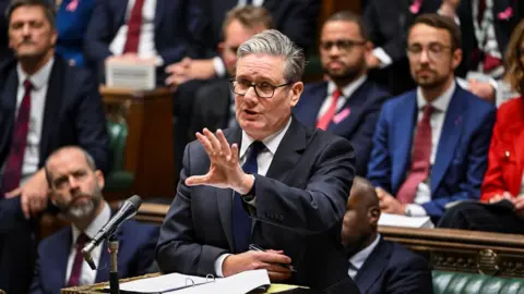 Reuters British Prime Minister Keir Starmer is gesturing from behind a podium, speaking at the House of Commons during the Prime Minister's Questions.
