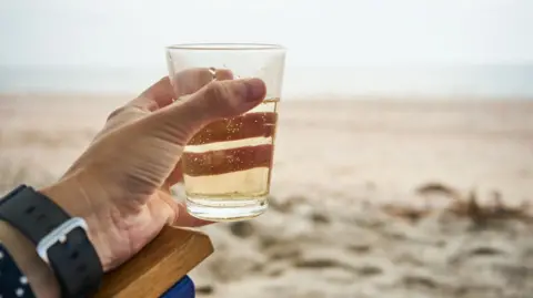 Getty Images Hand holding glass of drink on beach