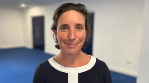 BBC Deputy Lindsay de Sausmarez - A woman with cropped brunette hair, smiling at the camera. She is wearing a black jumper with white trim. 