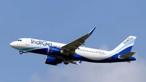 Getty Images An white IndiGo jet with the airline's blue livery flying with a clear sky in the background