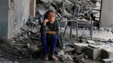 Reuters A Palestinian girl sits amid debris at a school in Gaza City's Zeitoun neighbourhood, where displaced people were taking shelter, after it was hit in an overnight Israeli strike (1 October 2025)