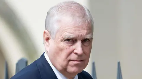 Getty Images A close-up of Prince Andrew, who is outside in front of some railings - he is wearing a dark blue suit jacket and a white shirt which can just be seen and is looking at the camera with a neutral expression 