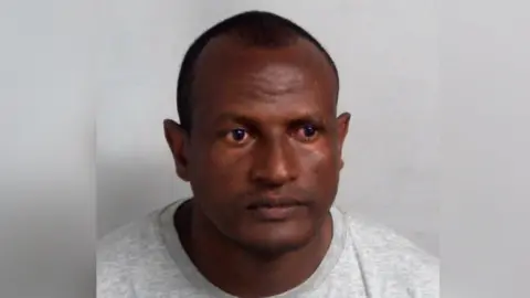 Essex Police A custody mugshot of Hadush Kebatu, who is wearing a grey sweater and has cropped black hair.