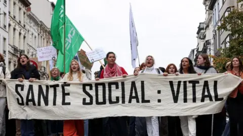 Reuters Protesters hold a banner as they attend a demonstration during a nationwide strike against the Belgian government's reform plans, in Brussels, Belgium, October 14, 2025.