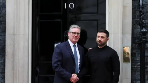 Reuters Sir Keir Starmer, wearing a blue suit, shaking hands with Ukraine's leader Volodymyr Zelensky, draped in all-black, outside the door of Number 10 Downing Street
